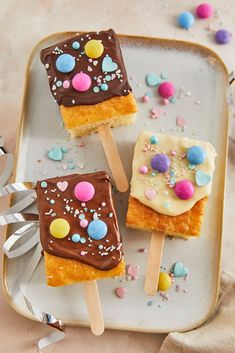 three marshmallow pops on a plate with sprinkles