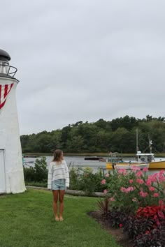 a woman standing in front of a lighthouse with flowers around her and boats on the water