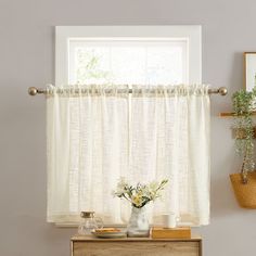 a white curtain hanging over a window next to a dresser and potted plant on top of it