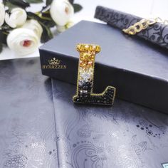 a black and gold necklace with a letter j on it sitting next to some flowers