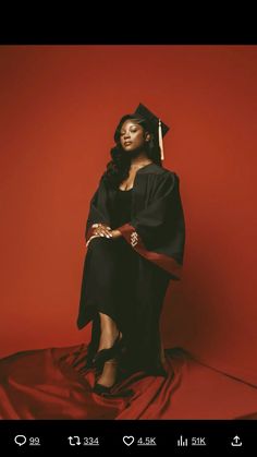 a woman sitting on top of a red sheet wearing a graduation gown and holding a tassel