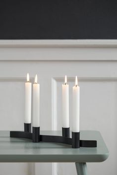 four candles are lit on a table in front of a white wall and black frame