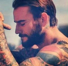 a man with lots of tattoos on his arm and chest looking down at his hand