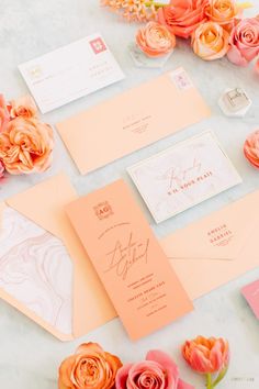 the wedding stationery is laid out on top of the table with pink and orange flowers