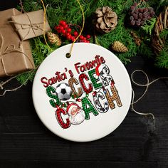 a white ornament with santa's favorite soccer coach on it next to presents