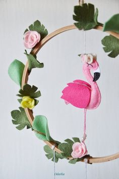 a pink flamingo is hanging from a wooden hoop with flowers and leaves on it