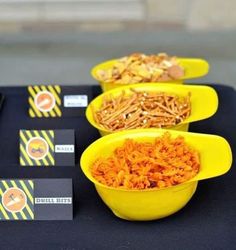 three yellow bowls filled with food sitting on top of a black table covered in signs