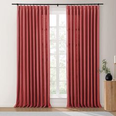 red curtains hanging on the side of a window in front of a white wall and wooden floor