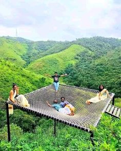 four people sitting on a hammock in the middle of a lush green valley