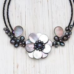 Black mother of pearl shell and peacock pearl wire-wrapped flower design Black glass seed beads Flexible/expandable memory wire, choker length Flower approximately 1.5" diameter Natural shells and pearls may vary slightly from photo Handmade in Thailand Adjustable Pearl Flower Necklace, Adjustable Mother Of Pearl Necklace With Round Beads, Adjustable Pearl Flower Beaded Necklace, Handmade Adjustable Flower Pearl Necklace, Adjustable Beaded Mother Of Pearl Necklace, Shells And Pearls, Wire Choker, Peacock Pearl, Choker Black