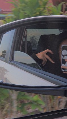 a woman taking a selfie in the side mirror of a car with her cell phone