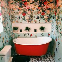 a red bath tub sitting in a bathroom next to a toilet and wall paper with flowers on it