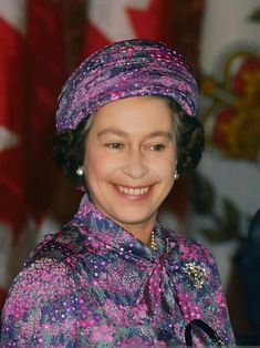 an older woman wearing a purple hat and smiling at the camera with canadian flag behind her