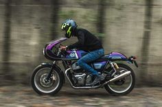 a man riding on the back of a purple motorcycle down a forest road with trees in the background