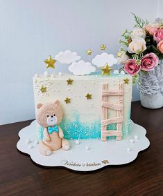 a teddy bear sitting on top of a cake next to a vase filled with flowers