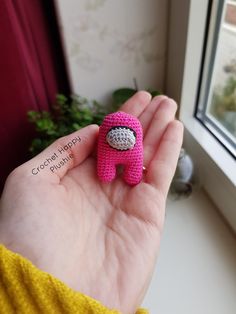 a small pink stuffed animal sitting on top of someone's hand next to a window