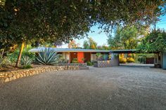 a house that is sitting in the middle of a driveway with trees and bushes around it