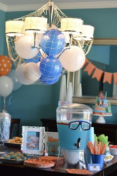 a blue and white party with balloons, decorations, and glasses on a table in front of a mirror