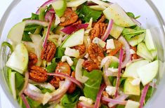 a salad with apples, onions and pecans in a glass bowl