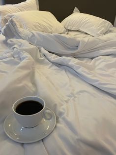 a cup of coffee sits on an unmade bed