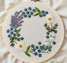 an embroidered wreath with blue flowers and green leaves is on a white sheet in the shape of a circle