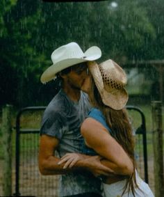 a man and woman kissing in the rain with hats over their heads on top of each other