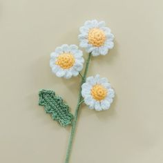 three crocheted flowers with leaves on a beige surface, one is yellow and the other is white