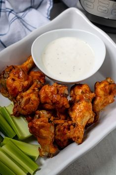 chicken wings and celery on a plate with ranch dressing next to it in a white bowl