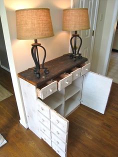 two lamps sitting on top of a wooden table next to a white cabinet with drawers