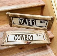 two wooden signs sitting on the side of a set of stairs that say cowgirl and cowboy way