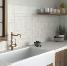 a white kitchen sink sitting under a window next to a counter top with bowls of fruit on it