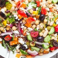 a white bowl filled with lots of veggies and chickpeas on top of a wooden table