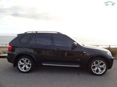 a black suv is parked on the side of the road by the water and beach