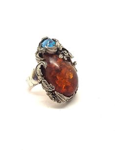 "What a stunning statement ring! Set with natural Amber and genuine Blue Topaz, this ring is truly a work of art. Handmade of sterling silver, the design features roses and flowing leaves. The Amber stone is large, about 35 mmm by 25 mm. The Blue Topaz is uniquely faceted. The whole setting is 1-3/4\" by 1-1/4\". The shank is a nice, heavy silver, 6 mm wide with a Claddagh design base. It appears to be signed, but unreadable. Unmarked, but guaranteed to be sterling silver." Unique Handmade Topaz Ring For Formal Occasions, Handmade Formal Topaz Ring, Unique Handmade Formal Topaz Ring, Handmade Topaz Rings With Unique Style, Unique Handmade Topaz Rings, Handmade Unique Topaz Rings, Unique Amber Wedding Rings, Natural Amber, Amber Stone