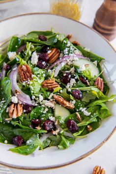 a salad with spinach, cranberries and pecans in a white bowl