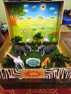 an open box filled with fake animals on top of a carpeted floor next to a wall