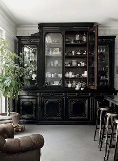 a black china cabinet with glass doors and shelves filled with dishes, cups, and vases