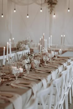 a long table with white chairs and candles