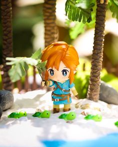 a figurine is standing in the sand near some palm trees and rocks,