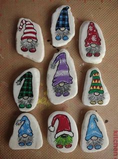 seven gnomes painted on white rocks sitting on a carpeted floor, each with different colored hats