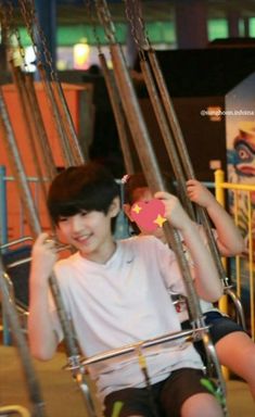 two young boys sitting on swings in an amusement park