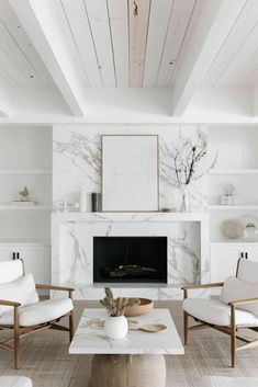 a living room with white furniture and a fireplace in the center, along with two chairs and a coffee table