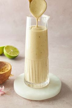 a small glass filled with liquid next to some sliced limes and a wooden spoon