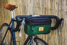 a blue bicycle with a green bag on it's front rack next to a bamboo wall