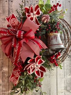 a red and white christmas wreath with a bell on the front door hanging from a wooden wall