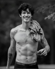 black and white photograph of a shirtless man with tattoos on his chest, smiling