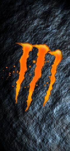 an orange and black monster logo painted on the side of a dark surface with water droplets