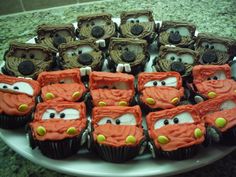 cupcakes with frosting decorated like cars on a white platter in front of a granite counter top