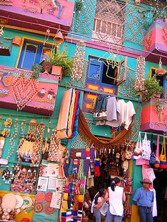 a colorful building with lots of different items hanging from it's sides and people walking by