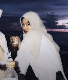 two women sitting at a table with drinks in front of them, both wearing white